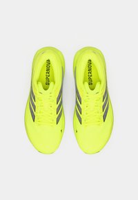 Lebendige gelbe Laufschuhe mit strukturierter Oberfläche, grauen Akzenten und sechs Ösen, auf der Zunge mit "SUPERNOVA" beschriftet.