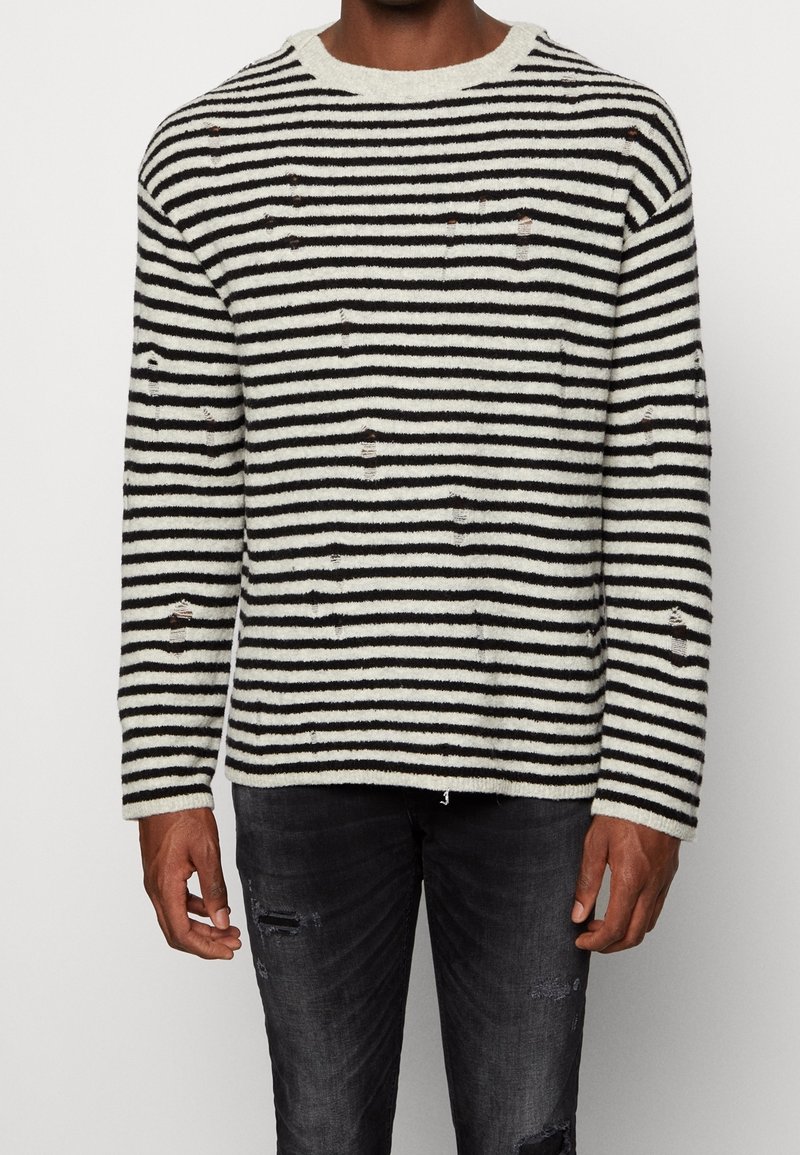 Sweter w paski w kolorze kremowym i czarnym o fakturowanym splocie, z przetarciami i okrągłym dekoltem. Połączony z ciemnymi, podartymi jeansami.