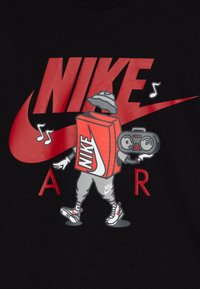 T-shirt negru cu un personaj de desene animate având un cutie Nike roșie pentru torace, pantaloni gri și un boombox, în fața unui logo mare Nike roșu.