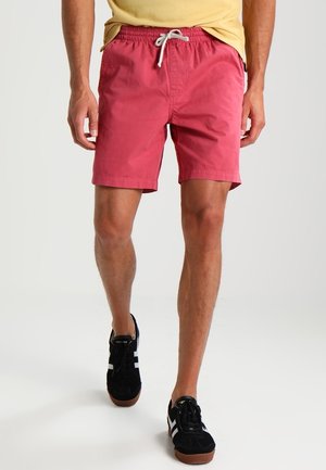 Røde bomuldsshorts med elastik i taljen og snøre, kombineret med sorte sneakers med hvide detaljer.