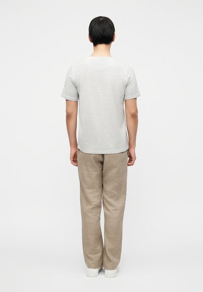 Γκρι κοντομάνικη μπλούζα και μπεζ λινό παντελόνι, εμφανίζονται από πίσω, με λευκά αθλητικά παπούτσια, σε απλό λευκό φόντο.