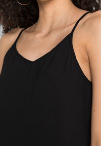 Czarny top na ramiączkach z cienkimi paskami i dekoltem w kształcie litery V. Wykonany z miękkiego, lekkiego materiału, charakteryzującego się gładką teksturą i minimalistycznym designem.