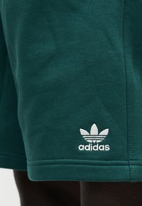 Πράσινα σορτς από απαλό ύφασμα με υφή στην επιφάνεια. Διαθέτουν λευκό λογότυπο Adidas στο κάτω τελείωμα και ραμμένο περίγραμμα.