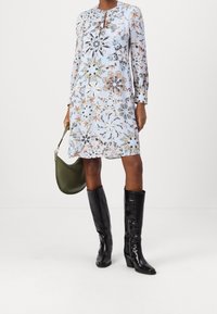 Vestido floral azul con mangas largas y escote en forma de llave, combinado con botas negras hasta la rodilla y un bolso verde olivo.