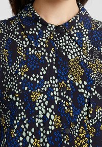 Camicia in tessuto nero con un motivo astratto colorato in blu, giallo e verde, dotata di colletto e bottoni neri.