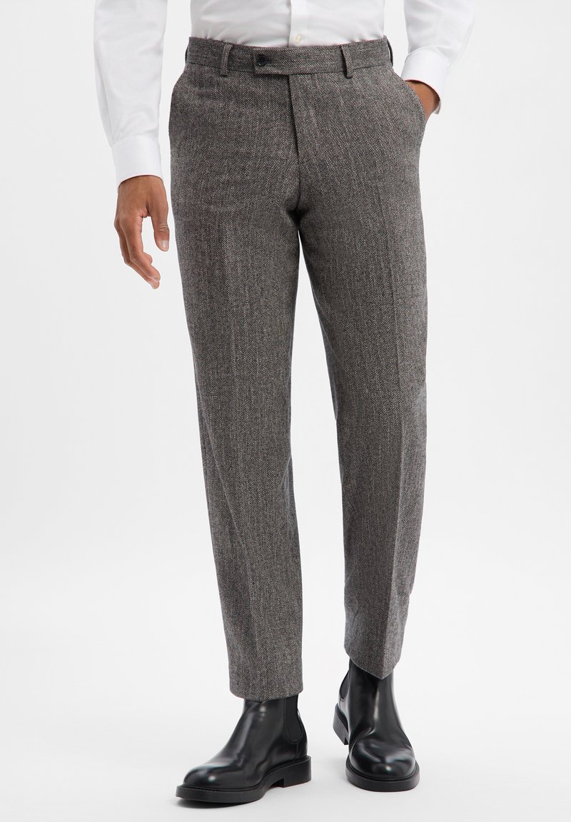 Spodnie z szarego materiału w wzór pepitki, o dopasowanym fasonie, z płaskim przodem i bocznymi kieszeniami, zestawione z czarnymi skórzanymi botkami za kostkę.