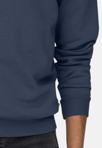 Sweatshirt bleu marine avec des poignets et un ourlet côtelés. Texture douce, coupe décontractée et détails de couture visibles. Convient pour une tenue décontractée.