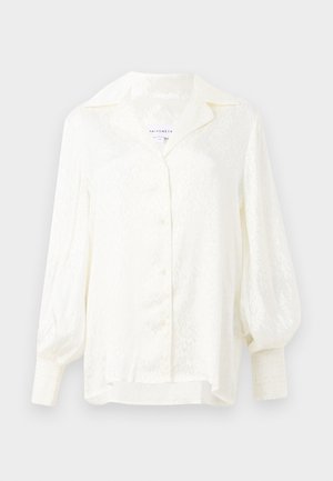 White blouse with a textured pattern, oversized collar, and puffed sleeves. Features button closure and smocked cuffs. Lightweight fabric.