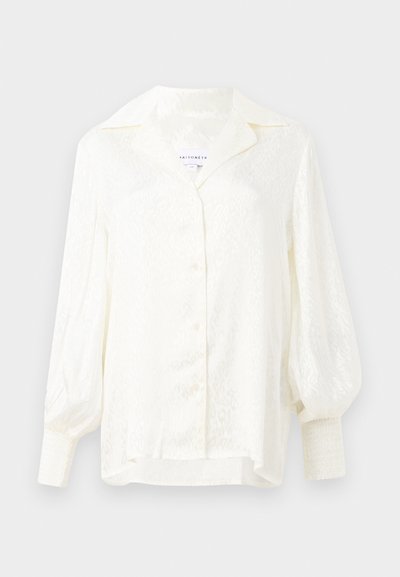 White blouse with a textured pattern, oversized collar, and puffed sleeves. Features button closure and smocked cuffs. Lightweight fabric.