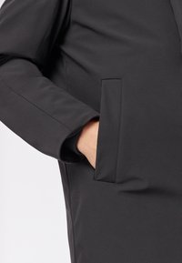 Czarna wodoodporna kurtka z gładką strukturą, boczną kieszenią i dopasowanym krojem, charakteryzująca się minimalistycznym stylem.