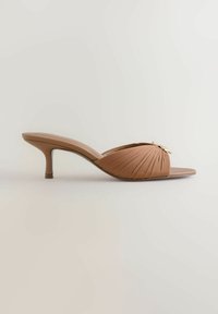 Mule en cuir marron à bout ouvert avec petit talon bas et dessus plissé orné d'un petit nœud doré sur fond neutre.