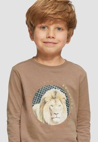Bruine langemouwen T-shirt met een centrale leeuwengrafiek omringd door een cirkelvormig groen raster en tekst in oranje en groene accenten.