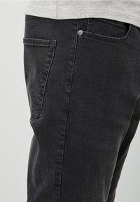 Mustat farkut, joissa on slim fit -leikkaus, hienovarainen rakenne, tavalliset taskut ja etunappi.