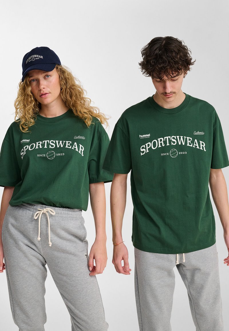 Donkergroene katoenen T-shirts met witte tekst "SPORTSWEAR", gecombineerd met grijze joggingbroek. Casual fit; geen zichtbare patronen of hardware-details.