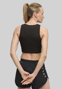 Sort ribbet crop top med rund halsudskæring, parret med sorte shorts med hvide logo accenter; set fra ryggen, hår i hestehale.