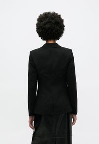 Μα ύρο ραμμένο σακάκι με μία σχισμή πίσω, δομημένους ώμους και γιακάδες με εγκοπές, συμπληρωμένο από απαλή υφή και εφαρμοστή σιλουέτα.