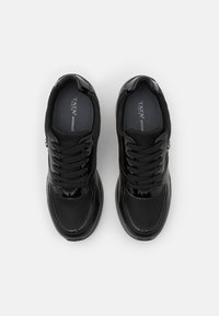 Pár černých dámských šněrovacích tenisek s lesklými detaily, polstrovanou stélkou a gumovou podrážkou, z pohledu shora na bílém pozadí.