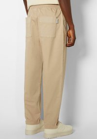 Beige bomullsbukser med en avslappnad passform, elastisk midja och två bakfickor. Kombineras med ljusa sneakers.