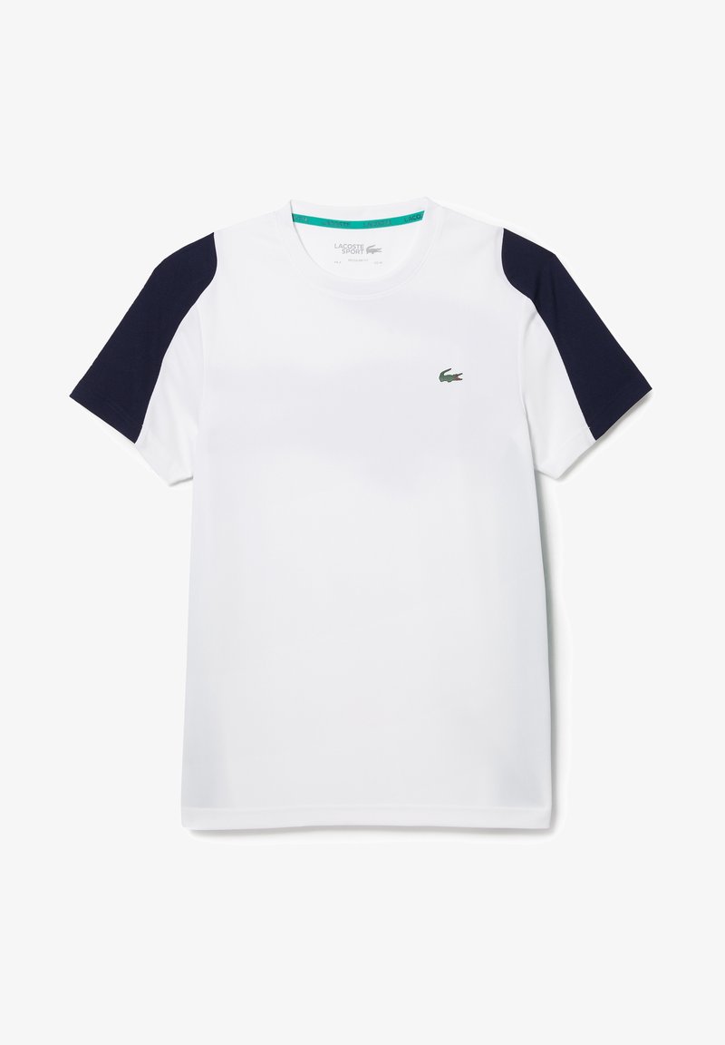 Vit sportt-shirt med mörkblå axelaccenter. Tillverkad av lättviktig tyg. Har en liten grön logotyp på bröstet.