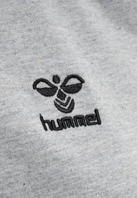 Grå bomullstyg med en svart broderad logotyp med en stiliserad biddesign ovanför texten "hummel" i fet stil.