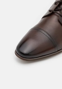 Chaussure habillée en cuir marron présentant un bout pointu, des coutures discrètes et une finition brillante. Design classique à lacets avec une silhouette élégante.