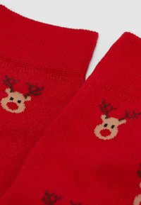 Rote Stricksocken mit kleinen Rentiergesichtern, die braune Geweihe, schwarze Augen und rote Nasen entlang des Stoffes zeigen.