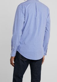 Niebiesko-biała koszula w kratę z długimi rękawami, mankietami na guziki i zaokrąglonym dołem. Tkanina wydaje się lekka o gładkiej fakturze.