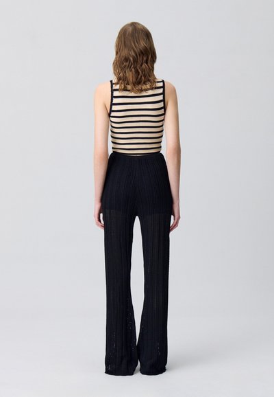 Débardeur en tricot rayé beige et marine, associé à un pantalon en tricot noir à jambes larges affichant un motif texturé et des détails en tissage ouvert.
