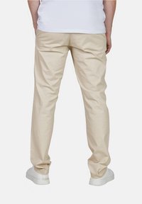 Beige Baumwollhose mit entspanntem Schnitt und geradem Bein. Kombiniert mit weißen Sneakers und einem schlichten weißen Hemd.