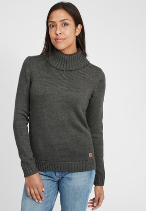 Dunkelgrauer Strickpullover mit hohem Kragen, geripptem Muster und einem kleinen Logo-Label am Saum. Wird mit blauen Jeans getragen.