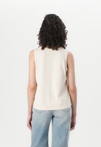 Top sin mangas beige con cuello redondo, material de algodón suave, ajuste ligeramente holgado y textura lisa, visto desde la parte trasera.