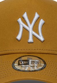 Προσαρμόσιμη καπέλο μπέιζμπολ New Era σε μουστάρδι κίτρινο, με λευκό κεντημένο λογότυπο "NY" και υφασμάτινη υφή. Στρογγυλή ετικέτα ορατή στο εσωτερικό.