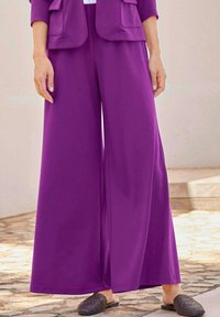 Pantalons larges violets en tissu lisse avec une coupe ample, dotés d'une taille haute et de poches latérales. Associés à des chaussures sombres à enfiler.