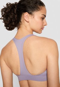 Soutien-gorge de sport violet clair avec un design à dos nageur, fabriqué en tissu lisse. Il présente une large bande et des détails de couture minimalistes.