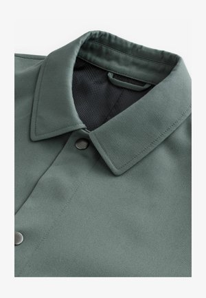 Kraeviste roheline särk, millel on tekstureeritud viimistlus. Särgil on must võrgusisustus ja nööbi sulg.