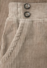 Béžové kordové kalhoty s ribbovou texturou, dvěma knoflíkovými uzávěry a detaily boční kapsy.