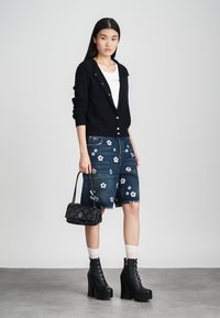 Juodas megztinis su mygtukų užsegimu, derinamas su mėlynomis džinsinėmis bermudomis, puoštomis baltomis gėlių siuvinėjimo detalėmis. Juodi aukštakulniai batai ir pūkuota rankinė.