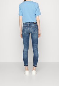 Jeans ajustados de mezclilla azul con un acabado desvanecido, detalles de costura y dos bolsillos traseros. Combinados con una camisa de manga corta azul clara y zapatillas blancas.