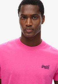 T-shirt di cotone rosa con maniche corte, scollatura rotonda e un piccolo logo ricamato sul lato sinistro del petto; tessuto liscio e di colore uniforme.