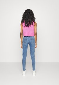 Top sin mangas de punto rosa, jeans skinny azules, zapatillas blancas de caña alta, visto desde atrás. Cuenta con una tela texturizada y un diseño típico de mezclilla.