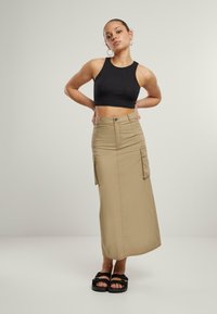 Khaki cargo maxi hame, jossa on sivutaskut, vyölenkit ja sileä pinta, yhdistettynä tiukkaan mustaan tanktoppiin ja mustiin sandaaleihin.