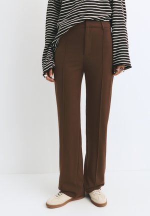 Pantaloni tailored marroni realizzati in un tessuto morbido con un design a gamba dritta. Abbinati a un top oversize a righe bianco e nere e scarpe da ginnastica color crema.