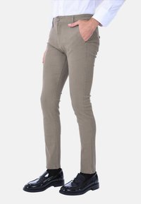 Pantaloni khaki slim-fit in tessuto texture, con tasche frontali e un design aderente, abbinati a mocassini neri lucidi.