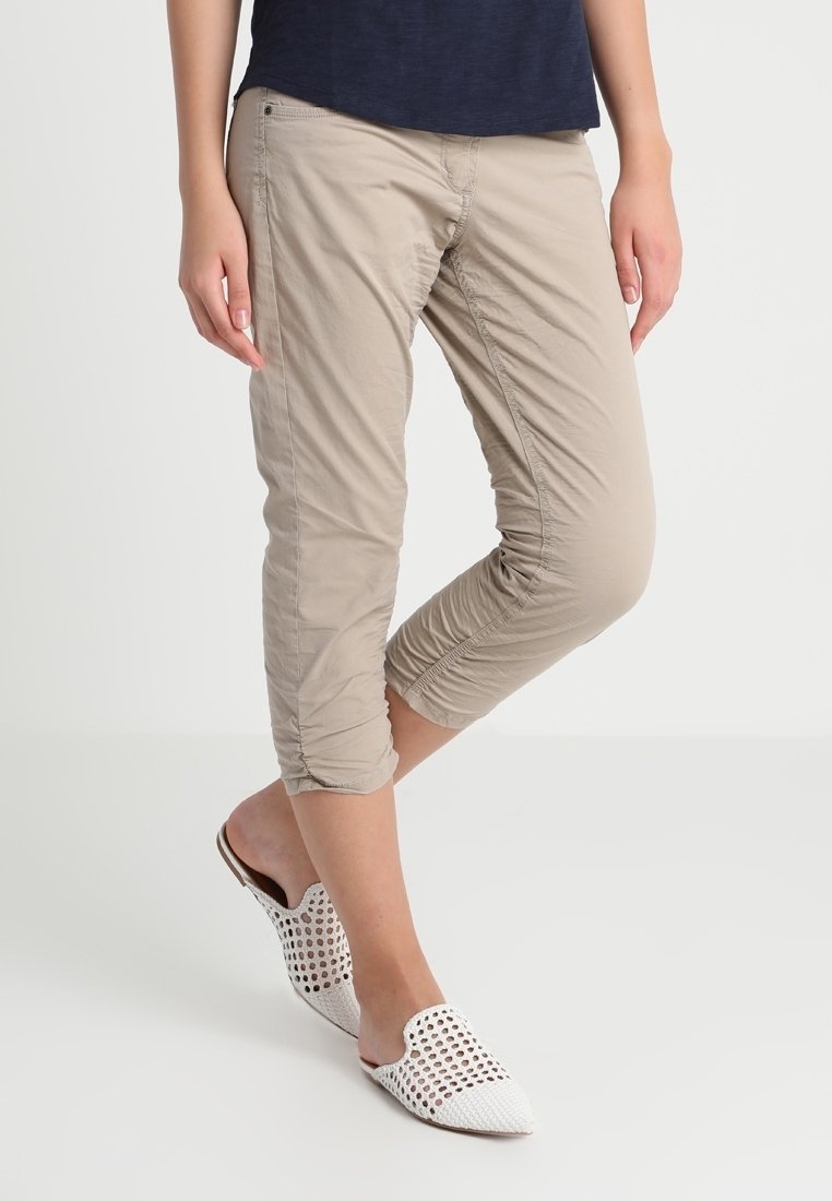 Beige cropped broek met gerimpelde zijnaden, gemaakt van lichtgewicht stof. Gecombineerd met witte perforated instapschoenen.