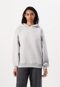 Felpa grigia con cappuccio regolabile, design comodo e maniche con polsini a coste. Indossata con pantaloni scuri a vestibilità rilassata. Tessuto morbido.