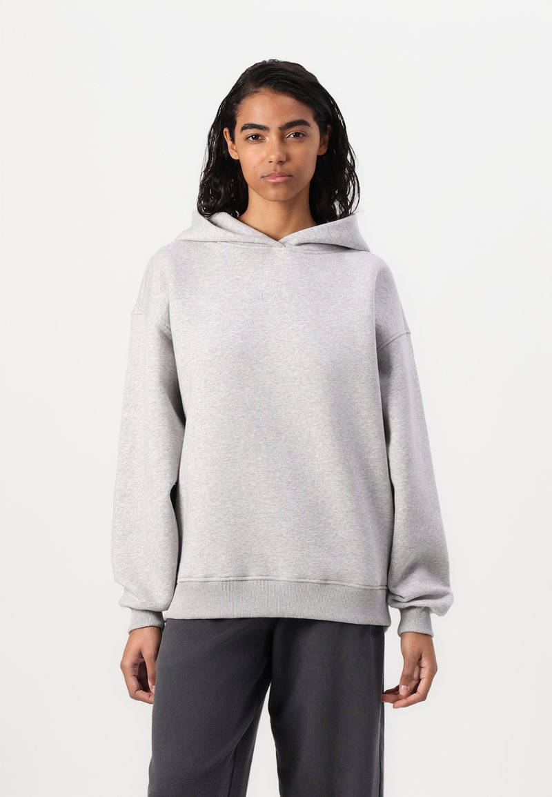 Felpa grigia con cappuccio regolabile, design comodo e maniche con polsini a coste. Indossata con pantaloni scuri a vestibilità rilassata. Tessuto morbido.
