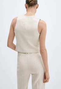 Beżowy top bez rękawów o prostym kroju, wykonany z teksturowanej tkaniny. Czyste linie i prosty design, zestawiony z pasującymi beżowymi spodniami.