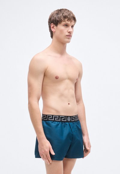 Μπλε σατέν μποξεράκια με μαύρη ζώνη μέσης που διαθέτει γεωμετρικό μοτίβο. Τα μποξεράκια έχουν άνετη εφαρμογή και ομαλή υφή.