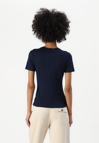 Navy blue cotton t-shirt with short sleeves, a round neckline, and a fitted shape, paired with light beige trousers featuring a button pocket.