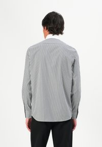 Striped shirt in black and white, featuring a pointed collar, long sleeves with buttoned cuffs, and a curved hemline. Minimalistic design.